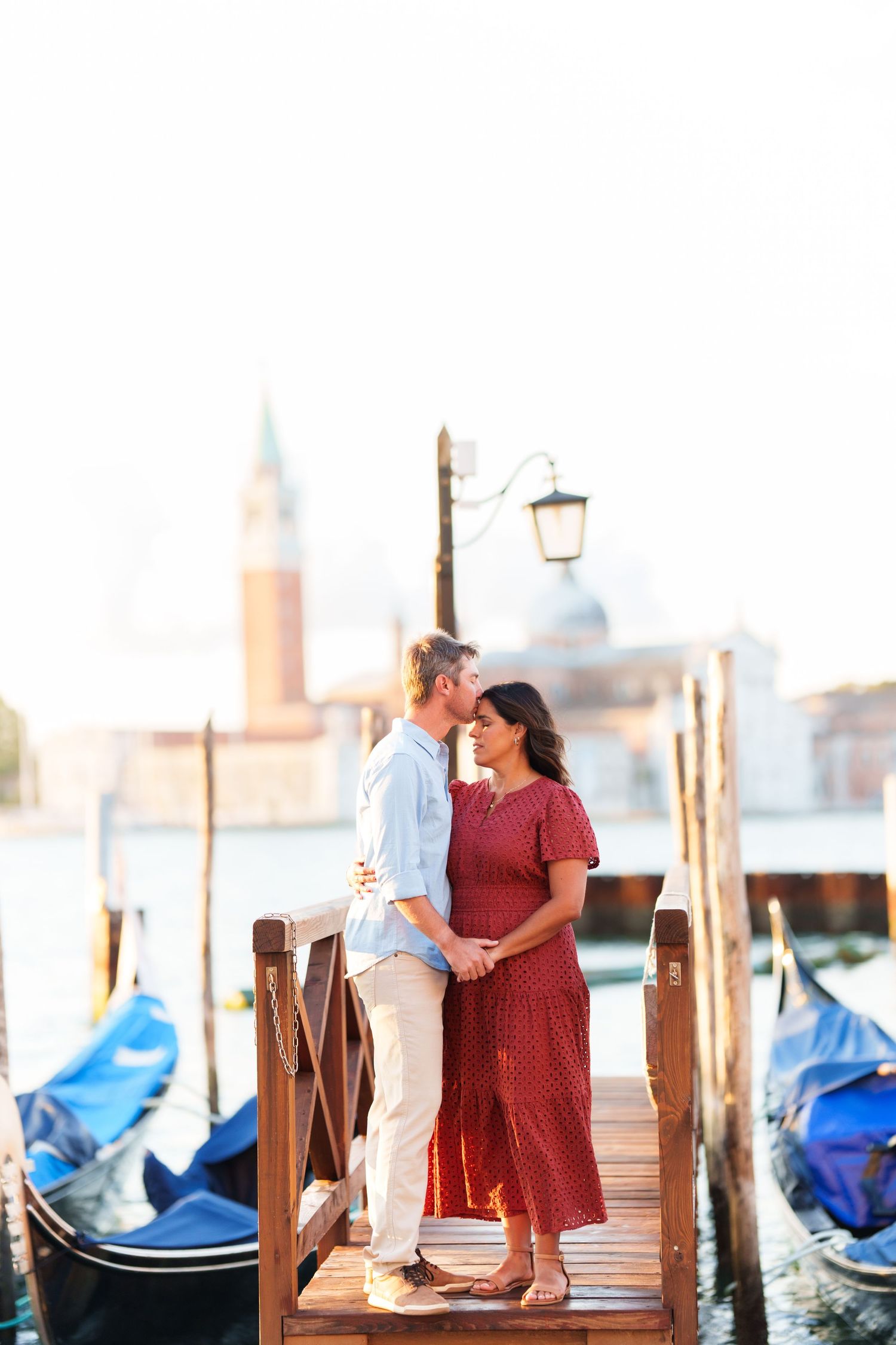 Romantic couple embracing on a Venice dock with gondolas and San Giorgio Maggiore church in the background.