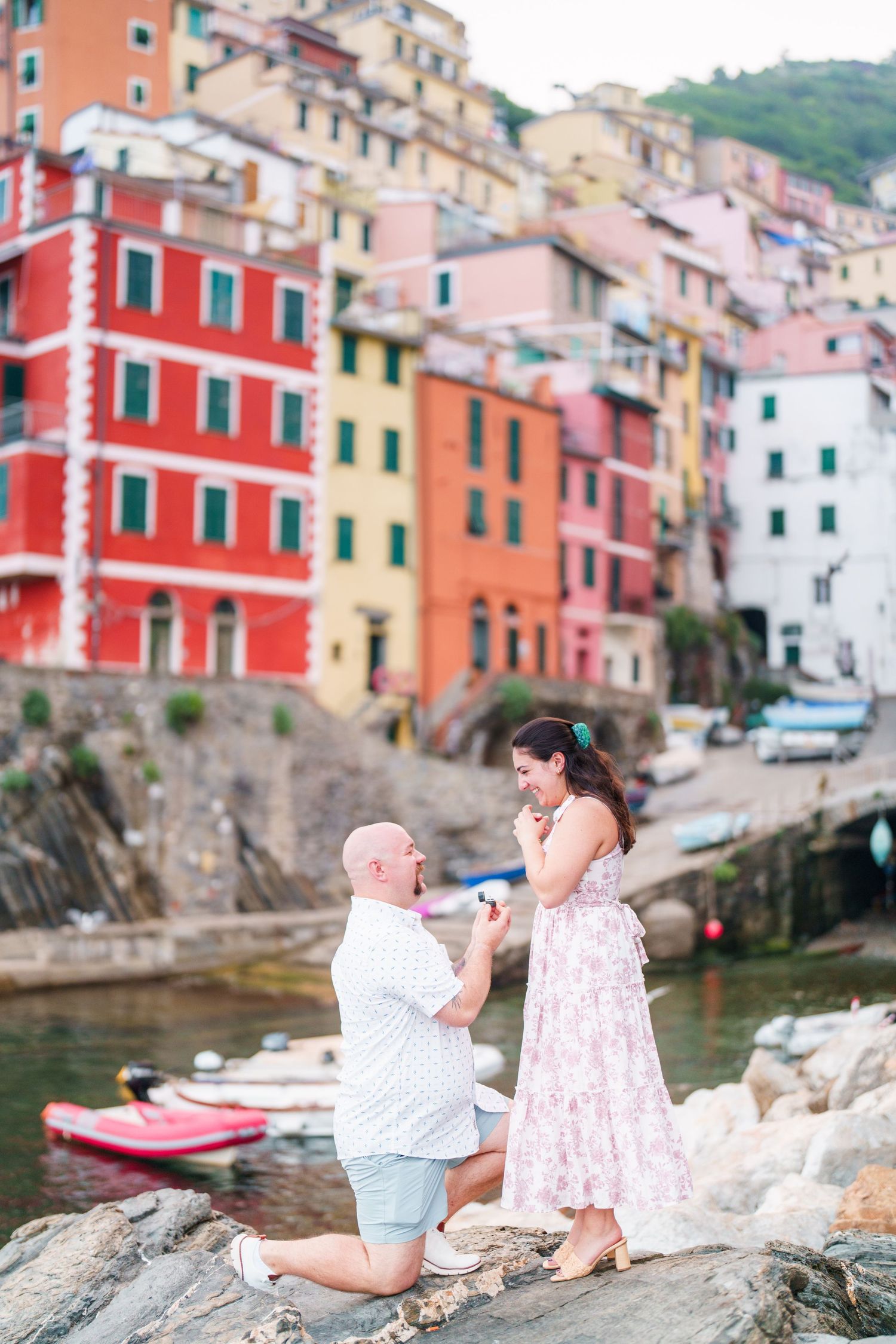 Man proposes on one knee to woman in front of colorful buildings of Riomaggiore, Cinque Terre, Italy.