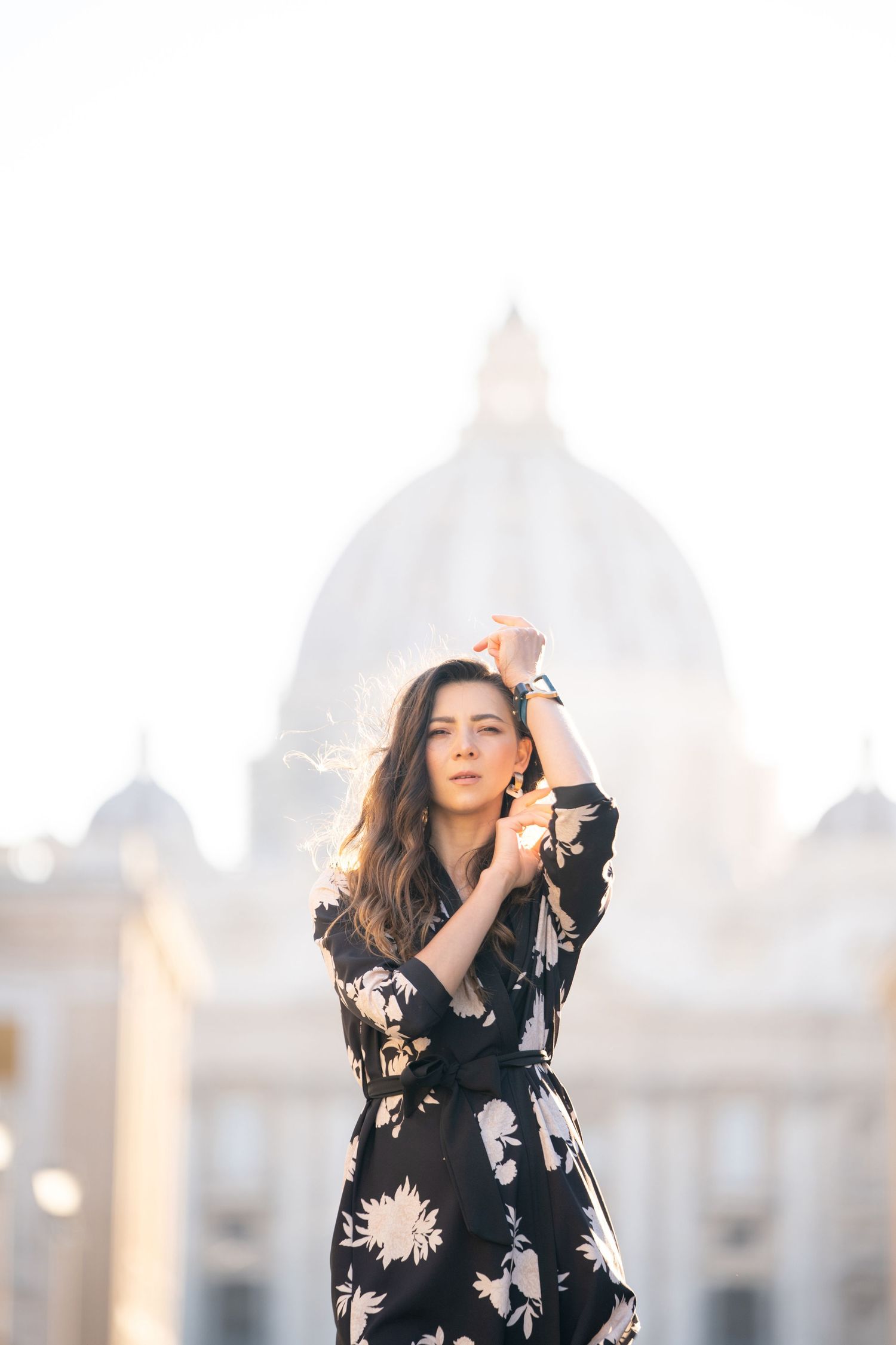 Woman in floral dress posing in front of St. Peter's Basilica dome in Rome, Italy.