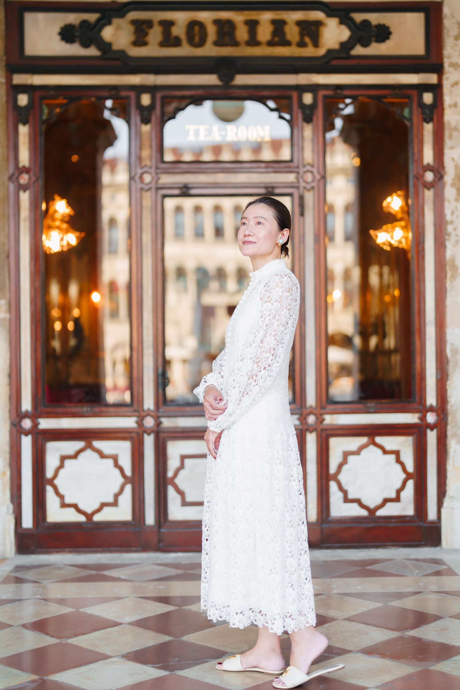 Woman in white lace dress standing outside Cafe Florian in Venice, Italy.
