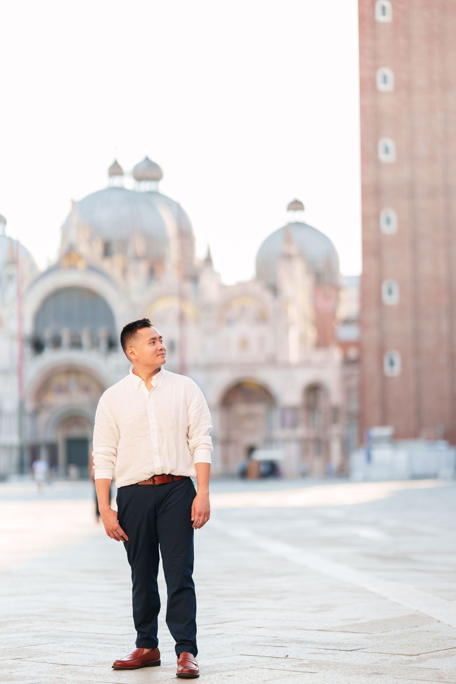 Man in white shirt and dark pants standing in St. Mark's Square, Venice, with the iconic basilica in the background.