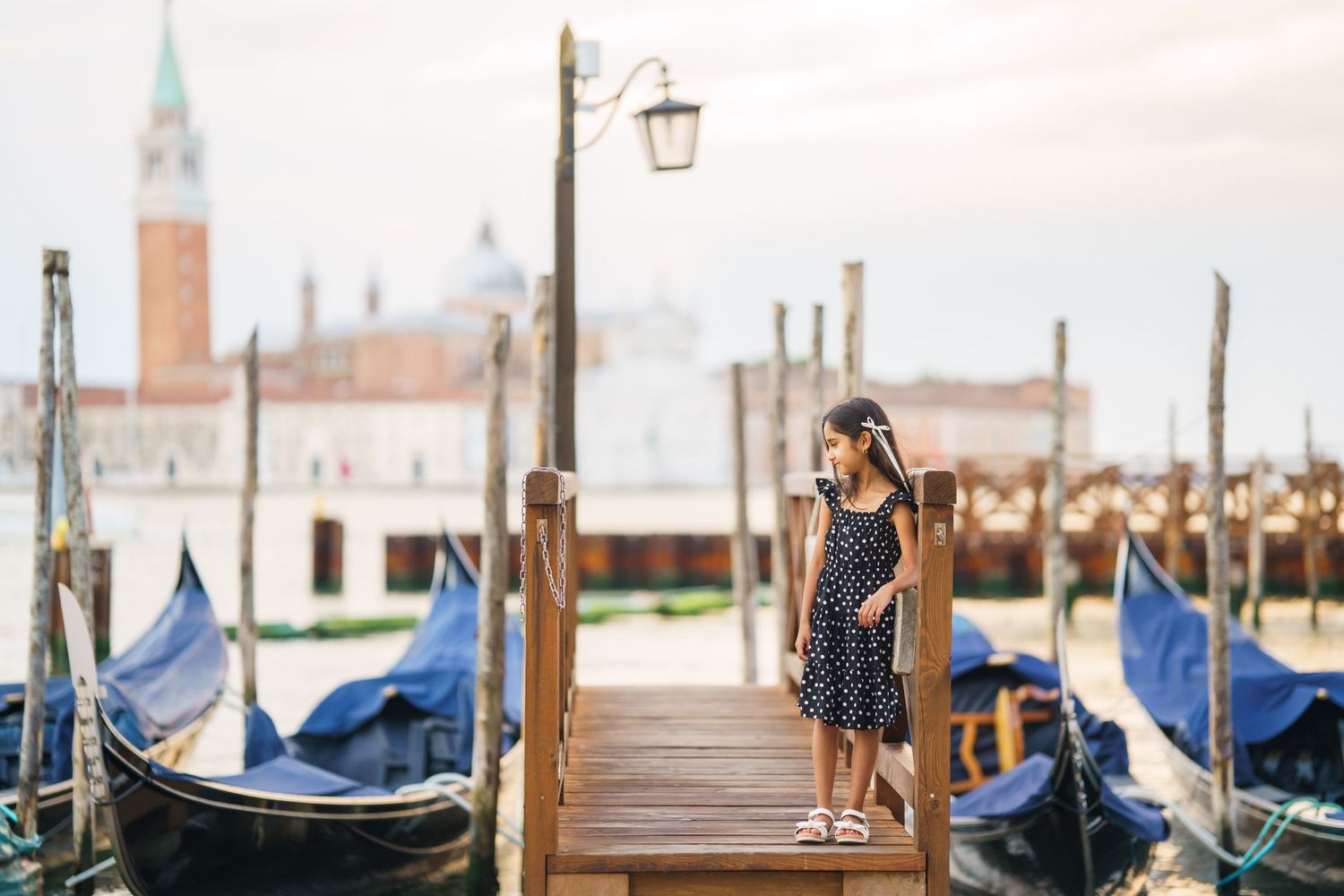 Young woman in polka dot dress standing on Venice gondola dock with San Giorgio Maggiore island in background.