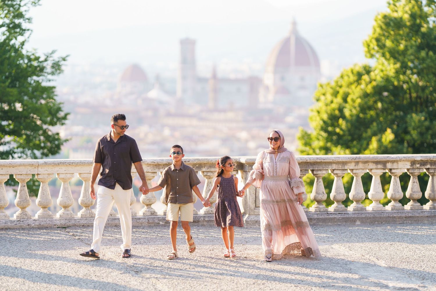 Family of four holding hands walking on a terrace with Florence Cathedral skyline backdrop in Italy.