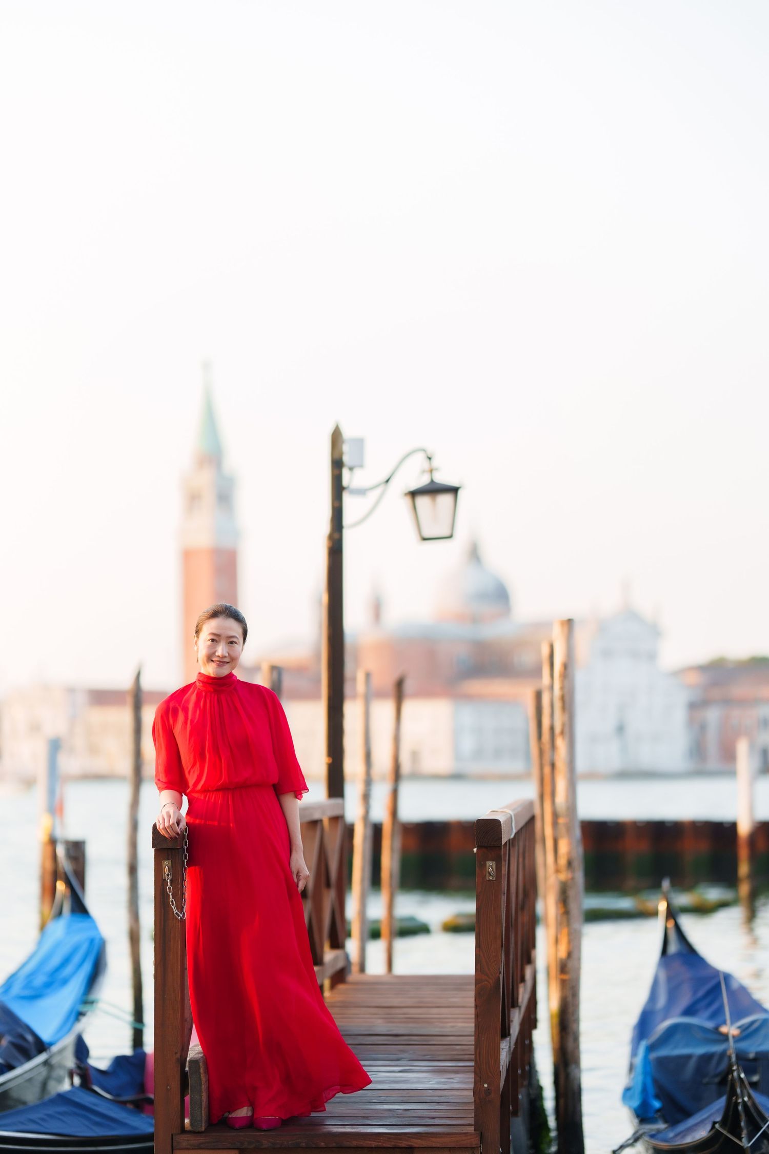 Woman in red dress standing on Venice gondola dock with San Giorgio Maggiore church in background.