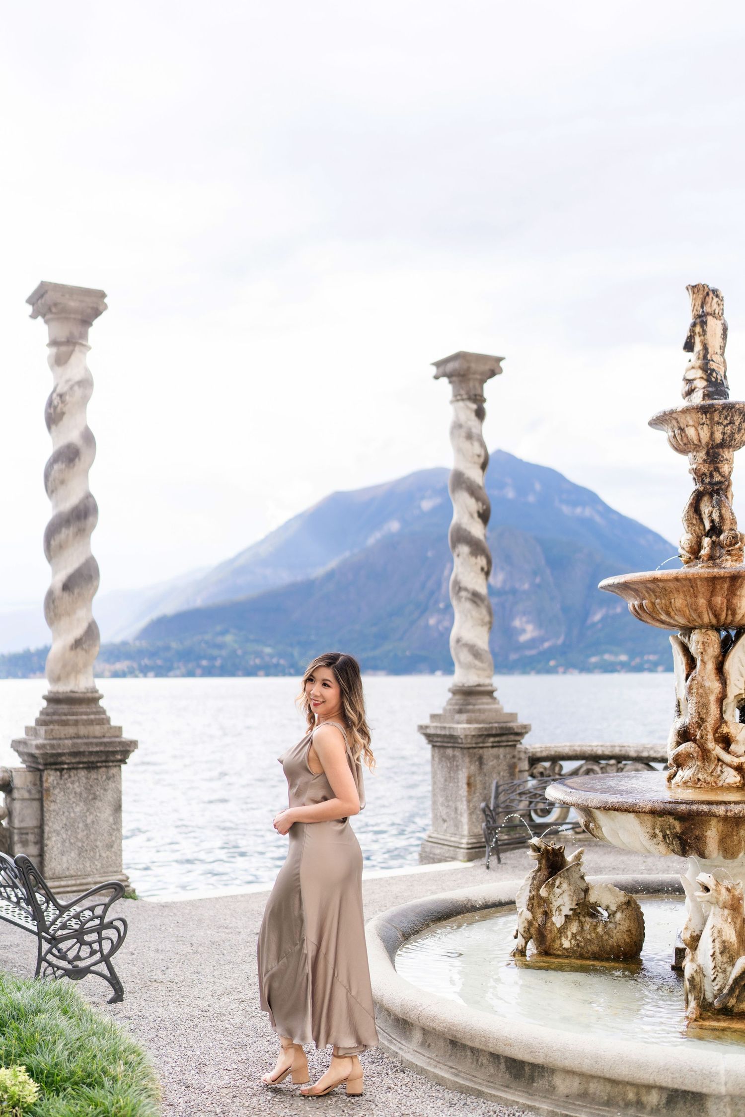 Ornate fountain and twisted marble columns frame scenic lakeside view with mountains in background at Villa del Balbianello.