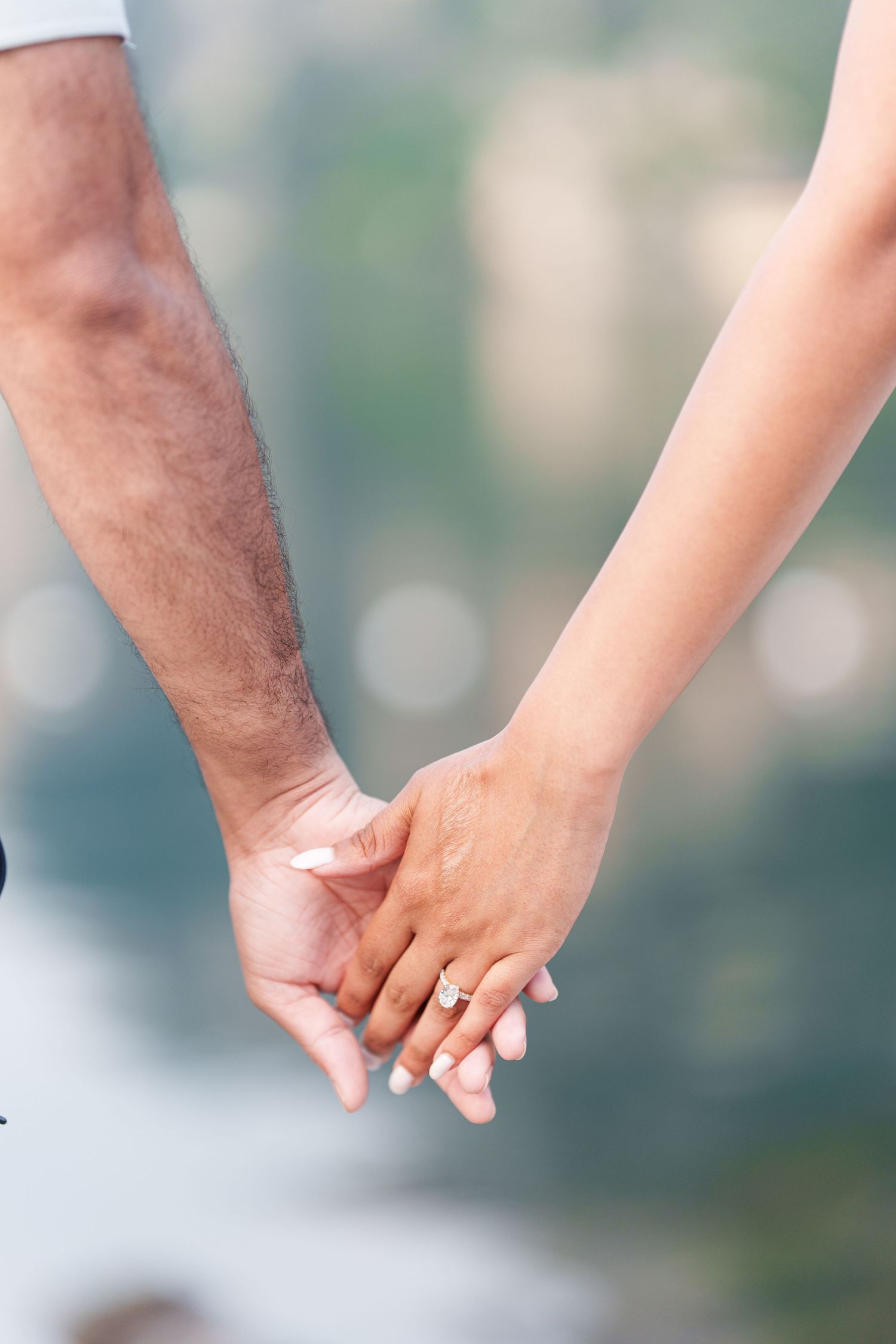 Close-up view of two people holding hands with contrasting skin tones against a soft blurred background.