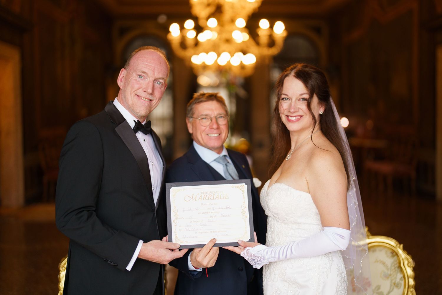Bride and groom share a joyful dance together during their wedding reception under elegant chandelier lighting.