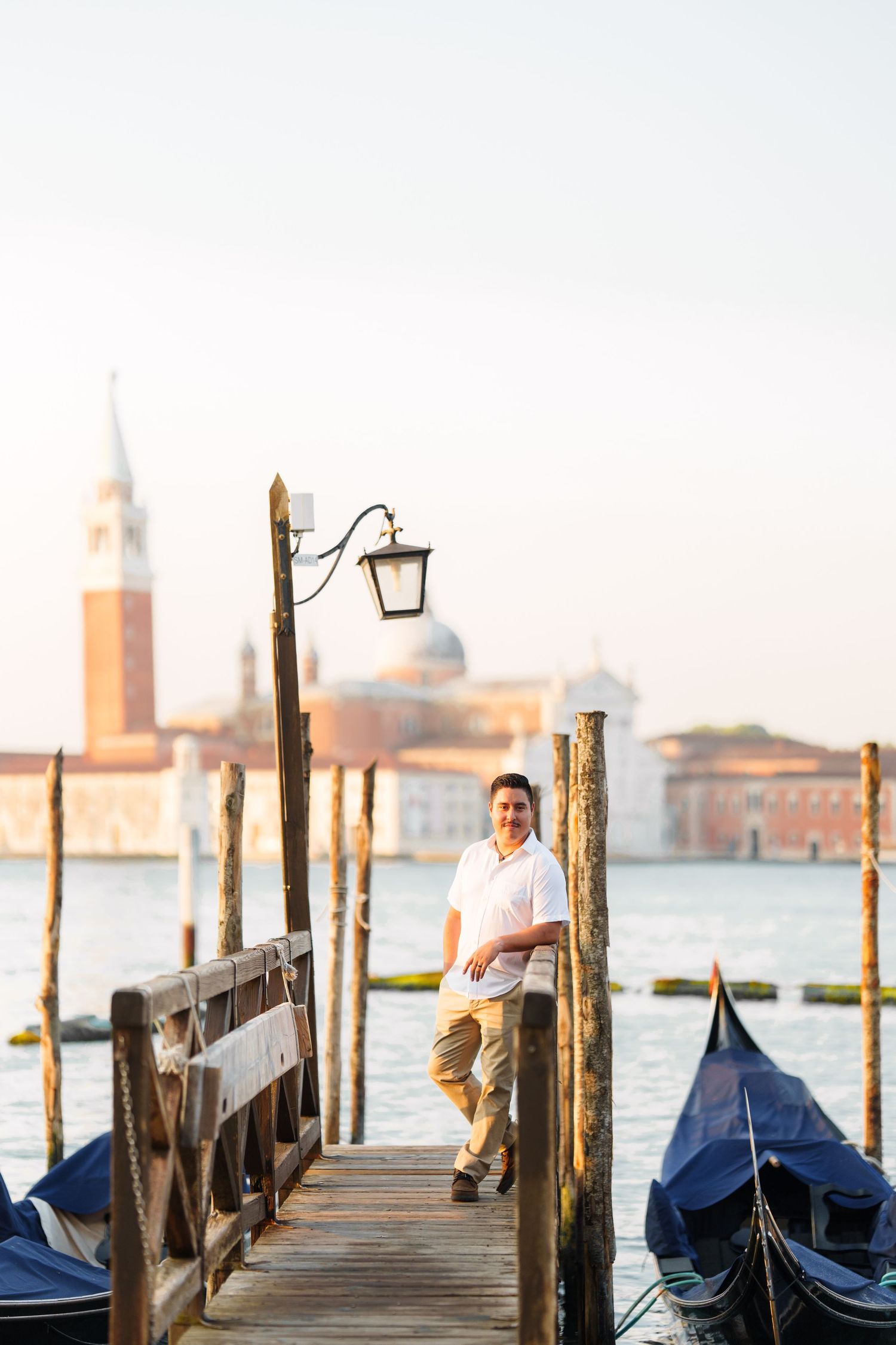photographer veniGondolas moored at a wooden dock in Venice with the iconic San Giorgio Maggiore church visible across the lagoon at sunset.