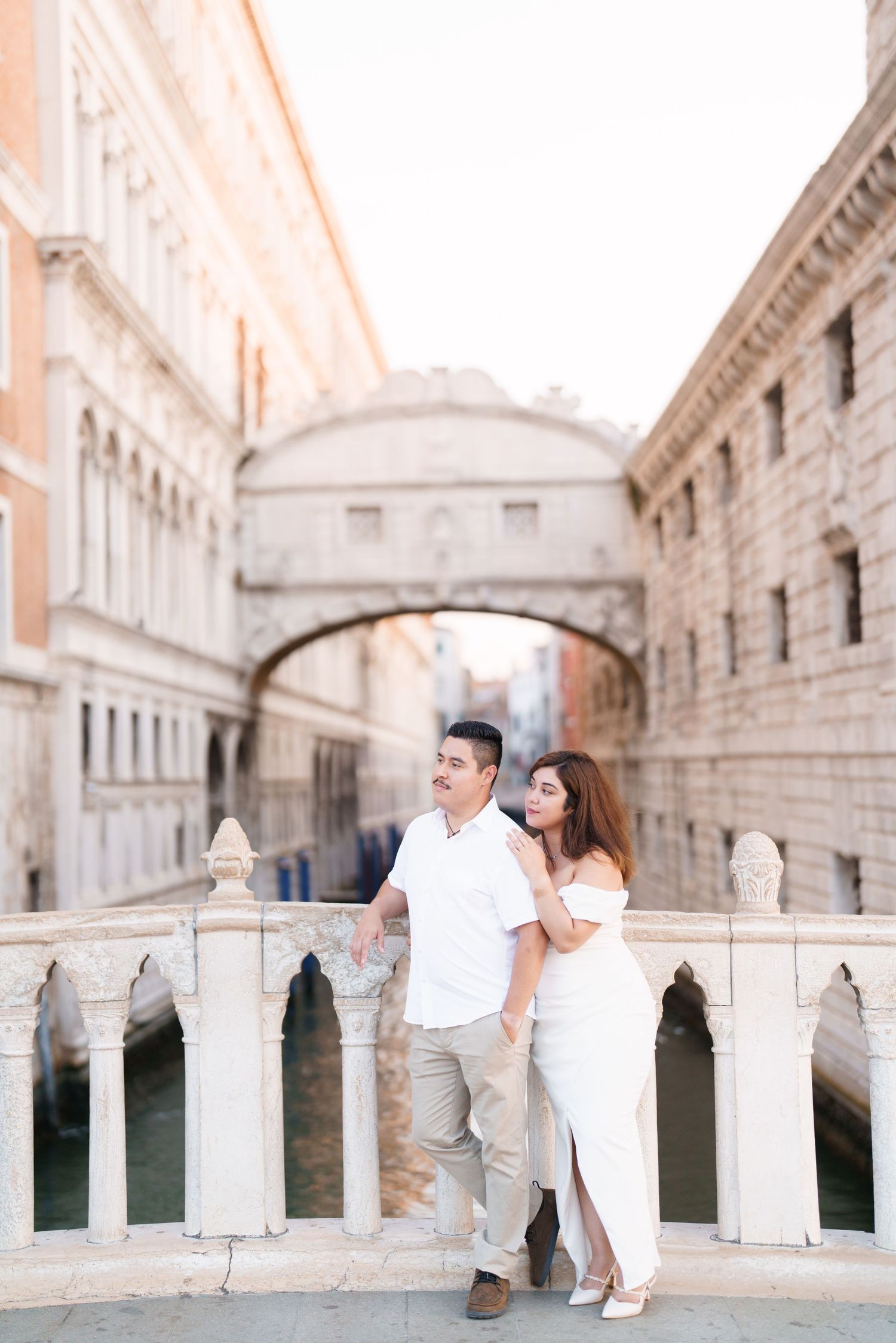 A couple sits together on the white marble Bridge of Sighs in Venice, Italy during a romantic photoshoot.