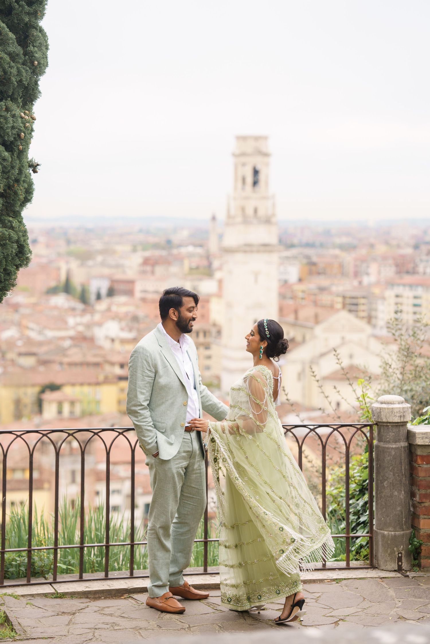 Couple shares romantic moments at a scenic overlook with Italian city rooftops and architecture in the background.