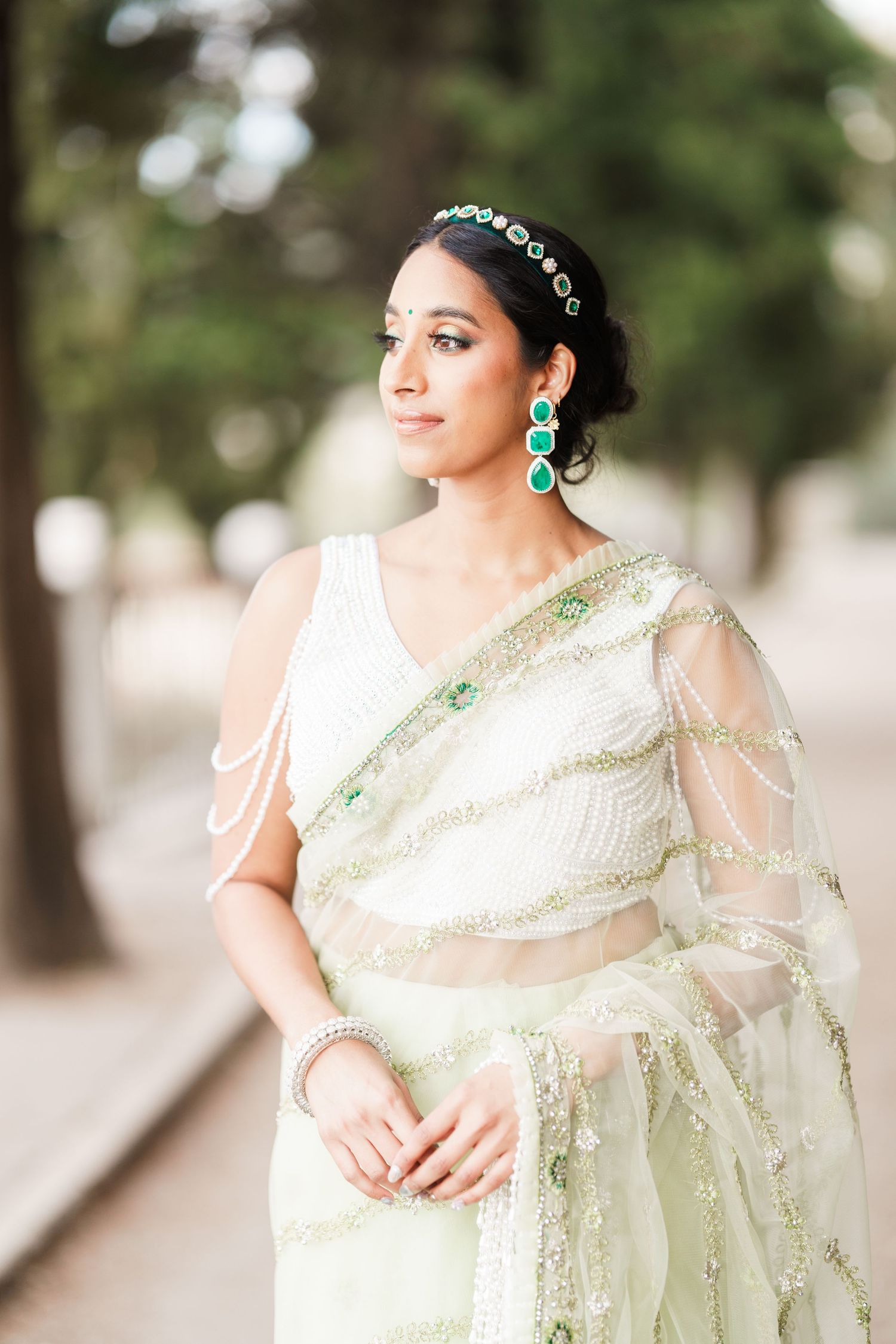 A bride in an elegant ivory and mint green saree with delicate embroidery poses gracefully against a soft blurred background.
