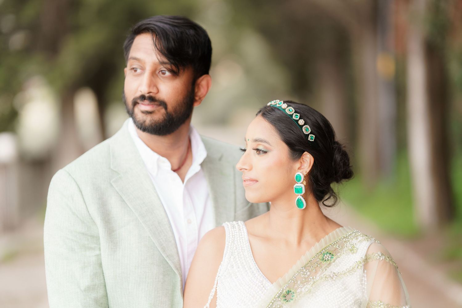 A couple in white wedding attire poses together in an outdoor garden setting.