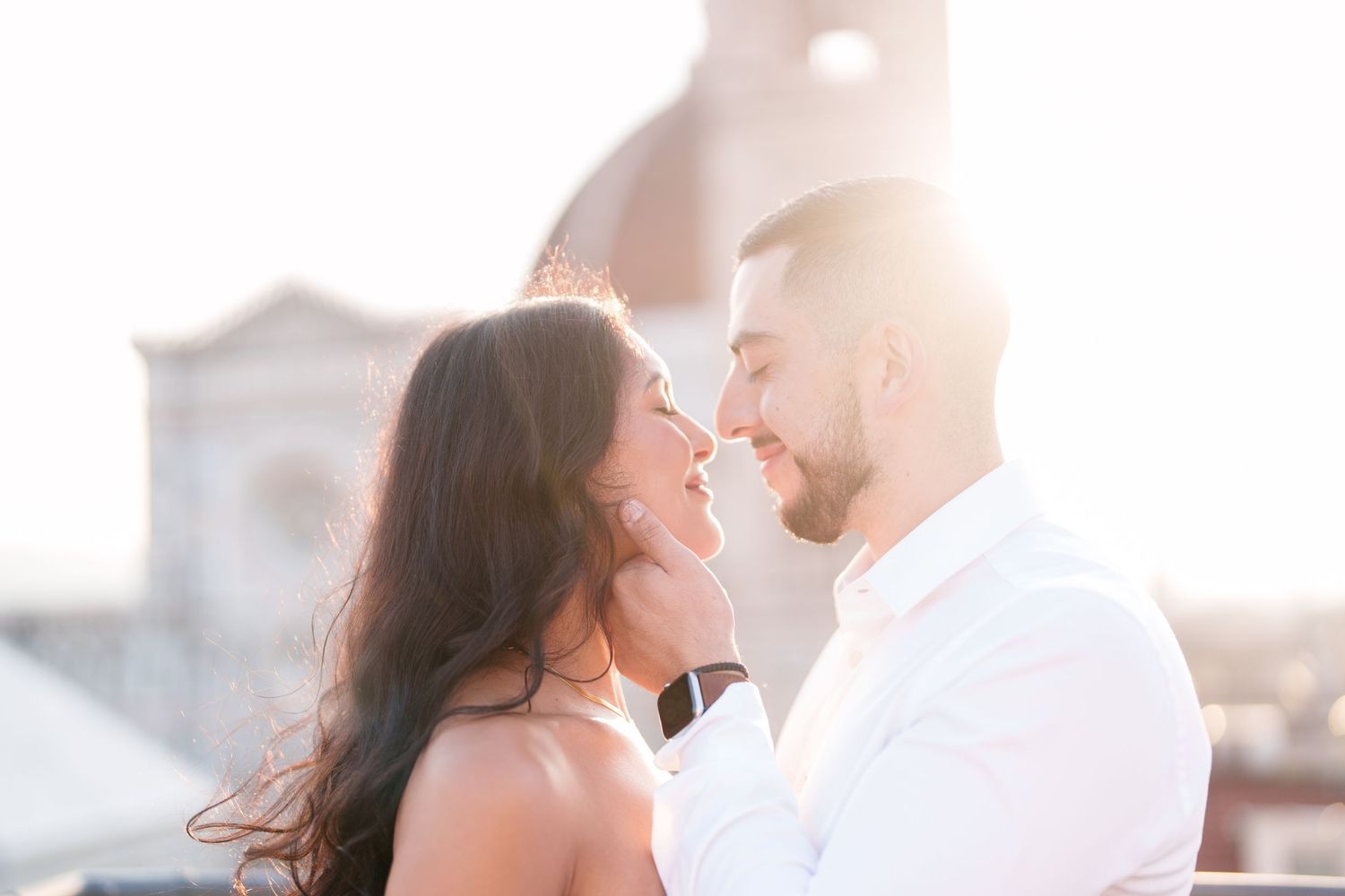 A couple embraces intimately during a golden sunset photo session on a rooftop.