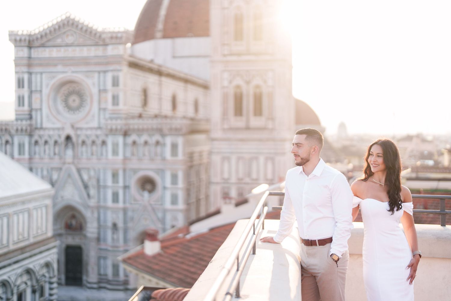 Couple in white outfits poses romantically at sunset in front of Florence Cathedral in Italy.