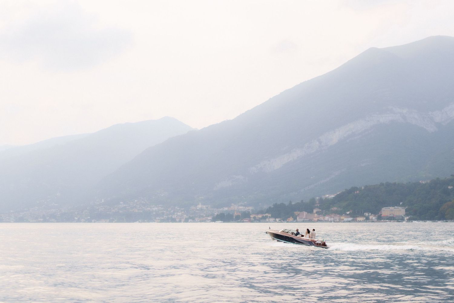 Scenic panoramic view of Lake Como in Italy with mountains and boats dotting the misty blue waters.
