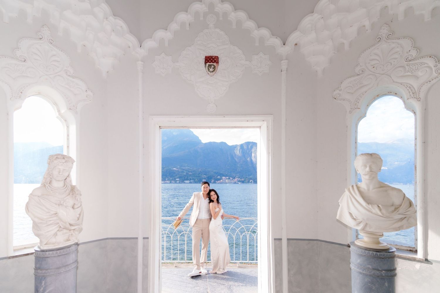 A romantic scene at Villa del Balbianello in Lake Como, framed by ornate white archways and marble statues.