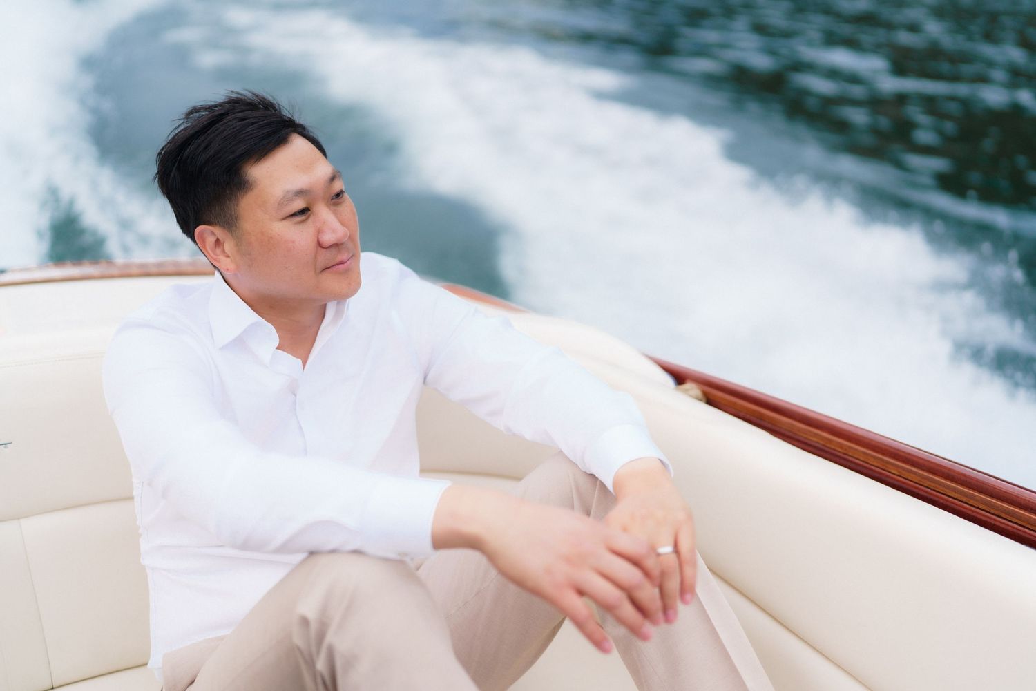 Person in white shirt relaxing on luxury boat with wake splashing behind on sunny day.