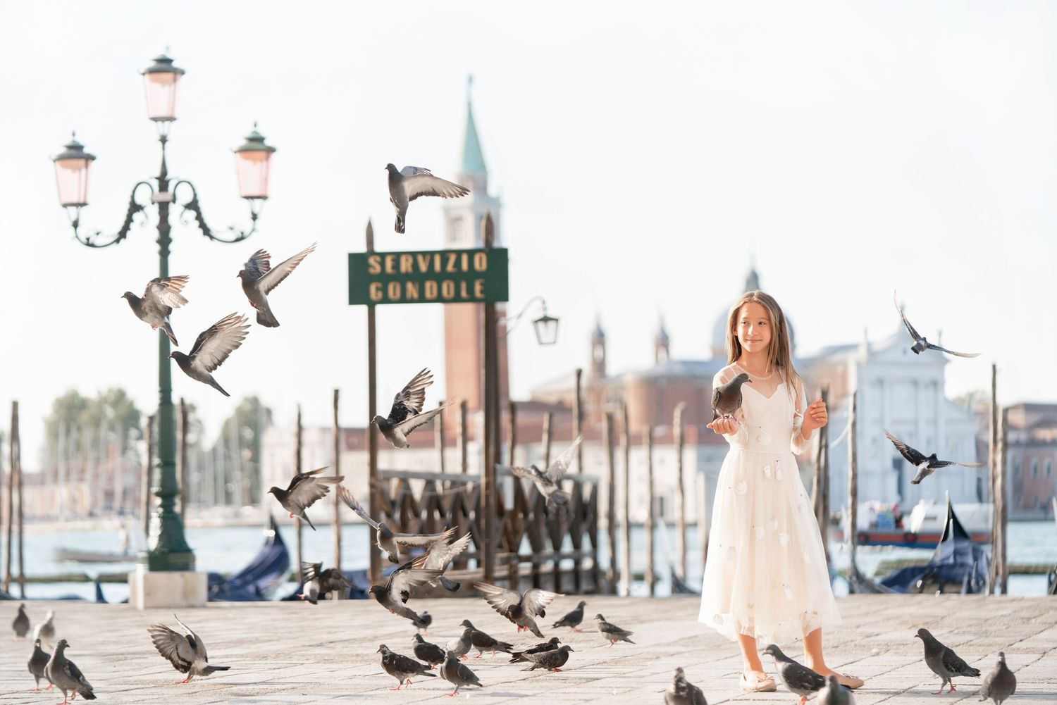 White dress and pigeons create a dreamy scene at Venice's St. Mark's Square with ornate lamp posts and basilica in background.
