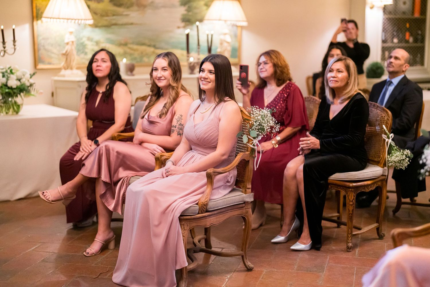 Wedding guests in pink and burgundy dresses seated in an elegant indoor venue.