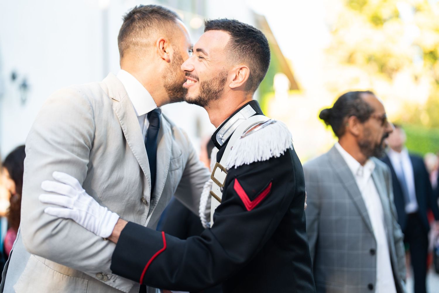A tender moment between two grooms in formal attire sharing their first kiss at a wedding celebration.