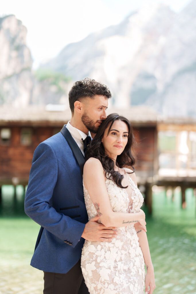 A tender moment between newlyweds by a lakeside boathouse in a stunning mountain setting.