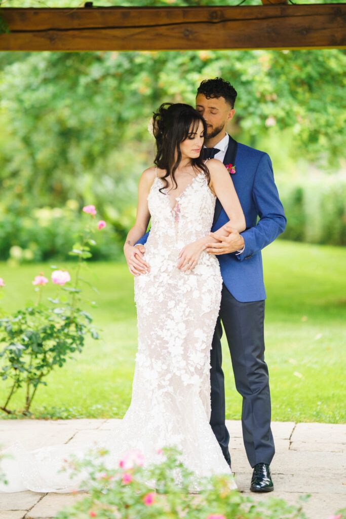 Intimate wedding portraits in a blooming garden with couple in blue suit and lace dress.