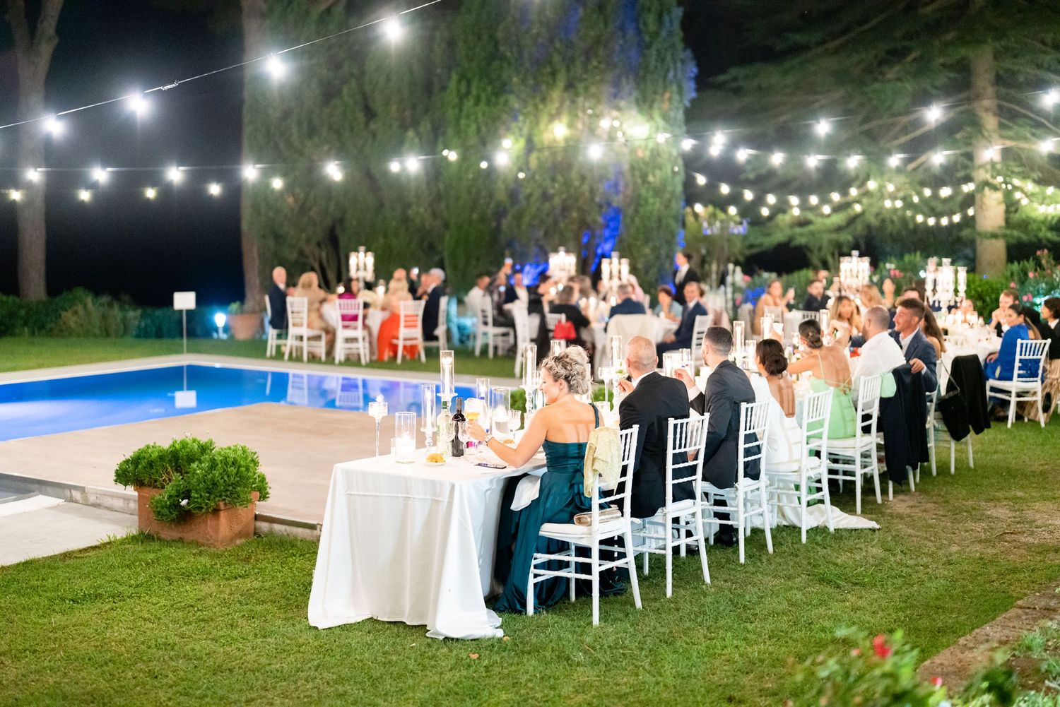 Evening outdoor wedding reception with white chairs and twinkling string lights illuminating the space.