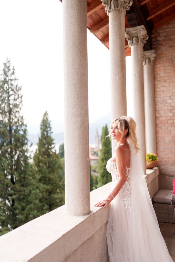 Bride in strapless gown poses against ornate stone columns with mountain backdrop.
