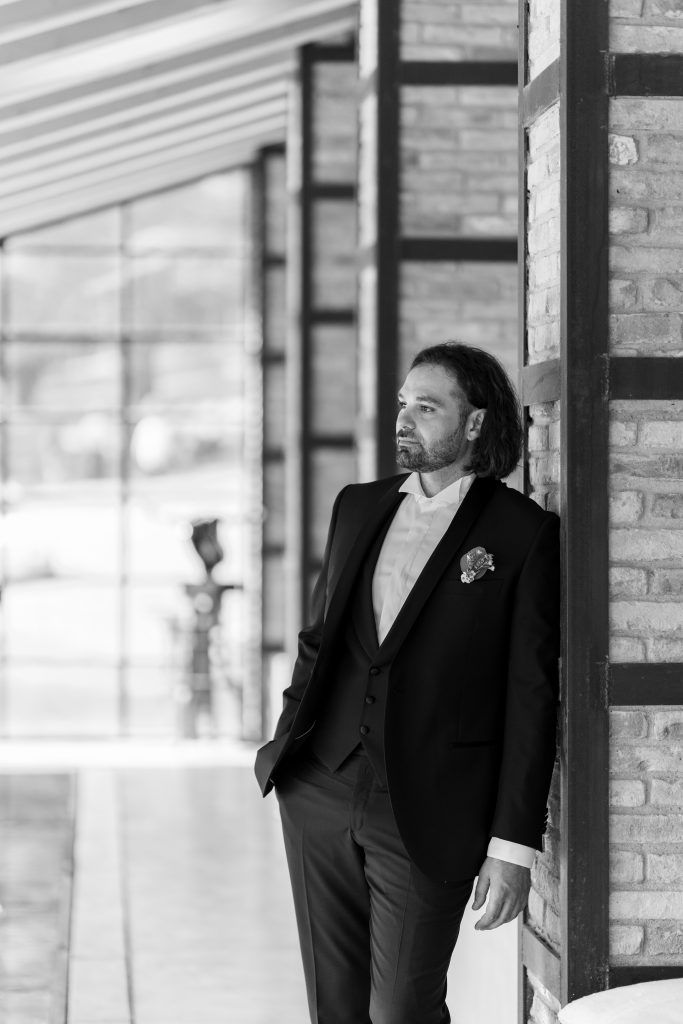 Black and white portrait of a person in formal attire leaning against a brick column.