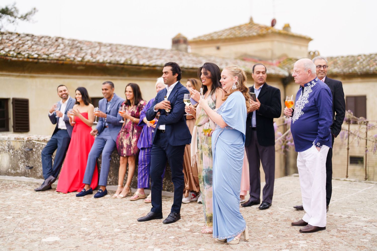 Wedding guests lined up for a group photo on a stone patio of a Mediterranean villa.