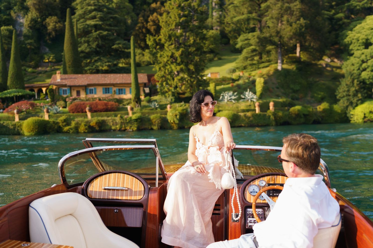 Couple enjoying a romantic boat ride on a serene lake surrounded by lush greenery and a charming villa.