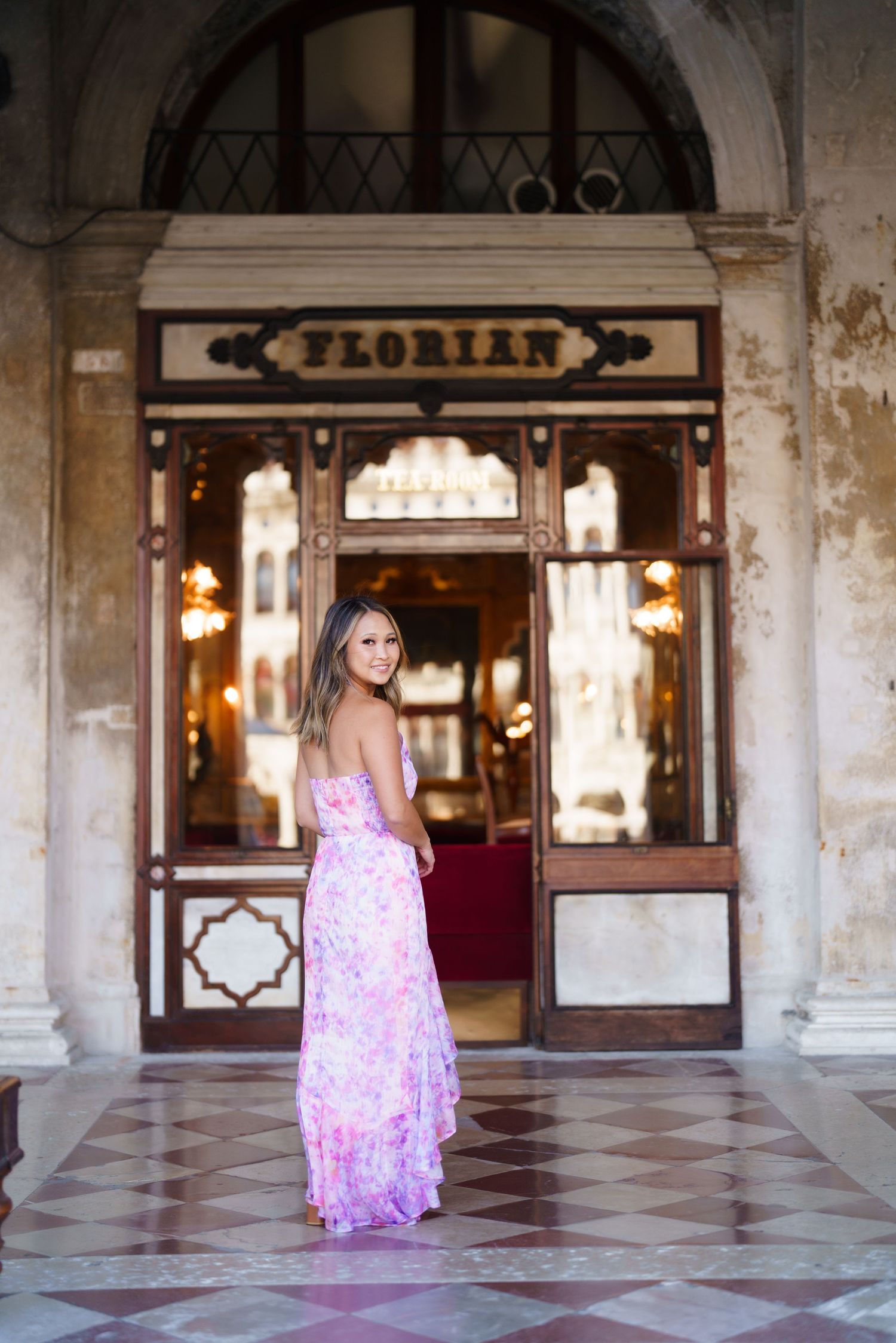 Woman in floral pink maxi dress posing outside Caffe Florian in Venice, Italy.