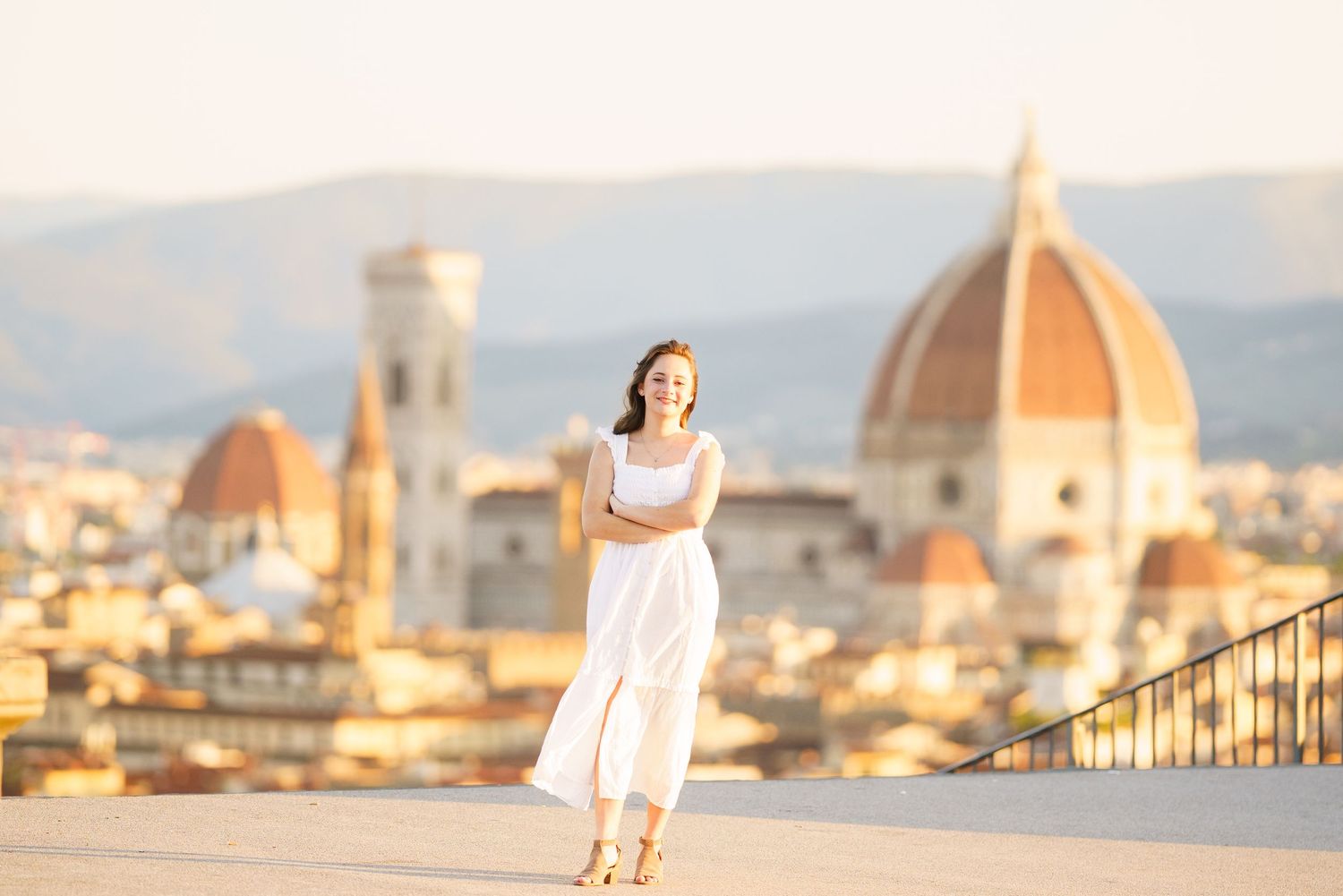 A woman in a white dress poses on a balcony overlooking the historic skyline of Florence, Italy with its iconic Duomo.