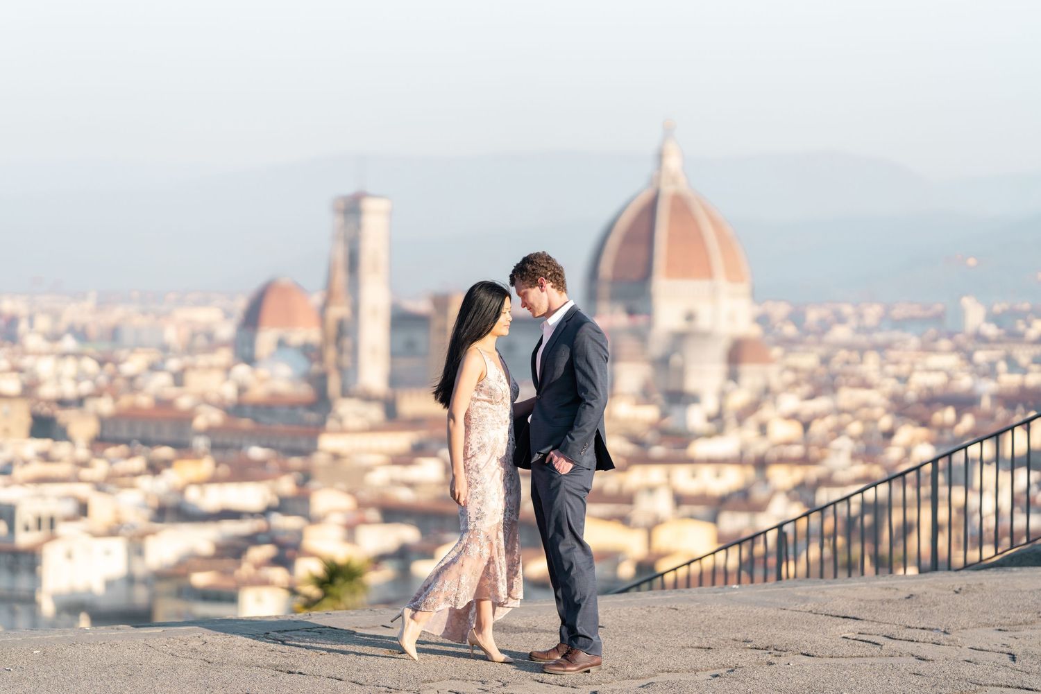 A couple shares a romantic moment overlooking Florence, Italy with the iconic Duomo cathedral dome in the background.