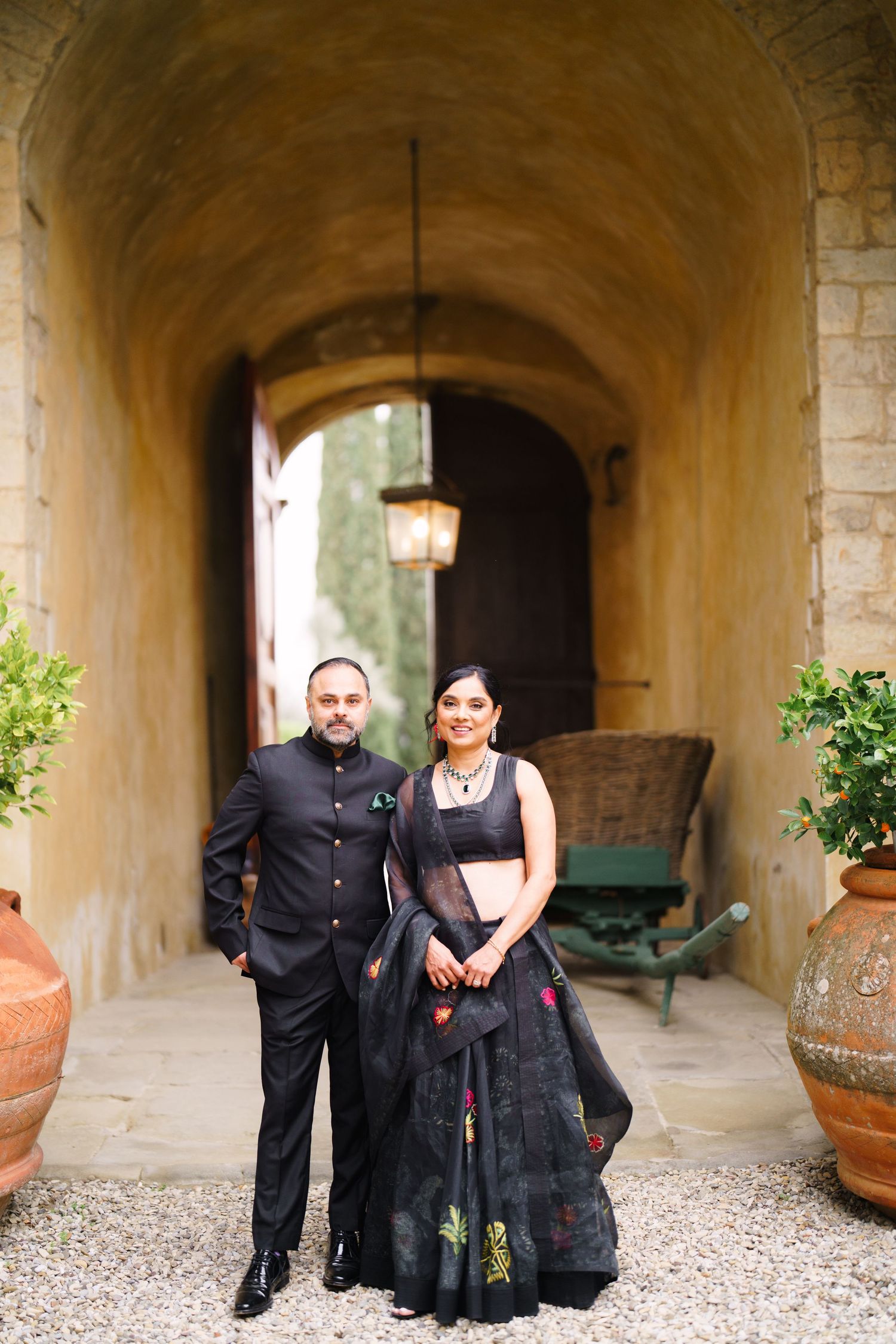 Couple posing together in an elegant stone corridor with arched ceilings and terracotta planters.