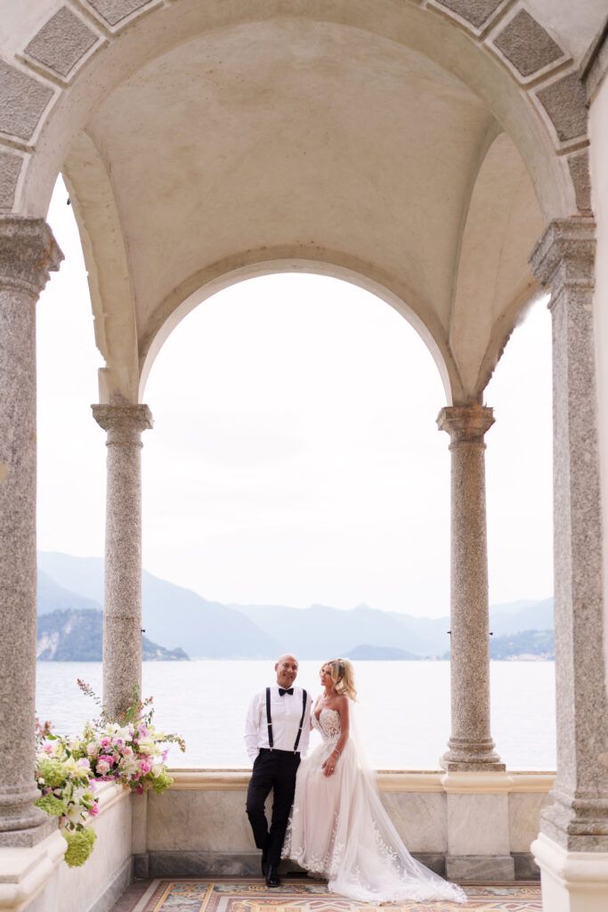 Romantic couple portrait under stone arches with mountain lake vista.