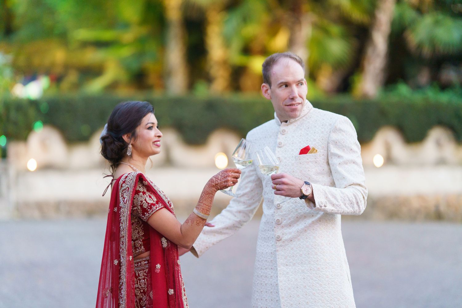 A couple in traditional Indian wedding attire dancing together in an outdoor setting.