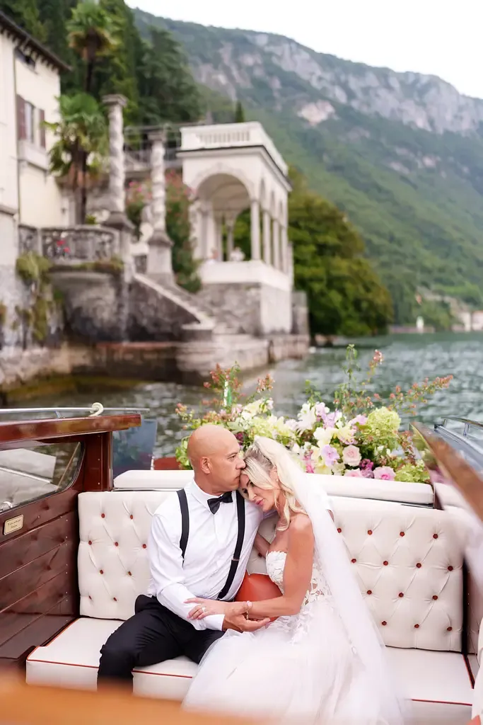 Newlyweds share romantic moment on cream sofa against scenic mountain lake backdrop.