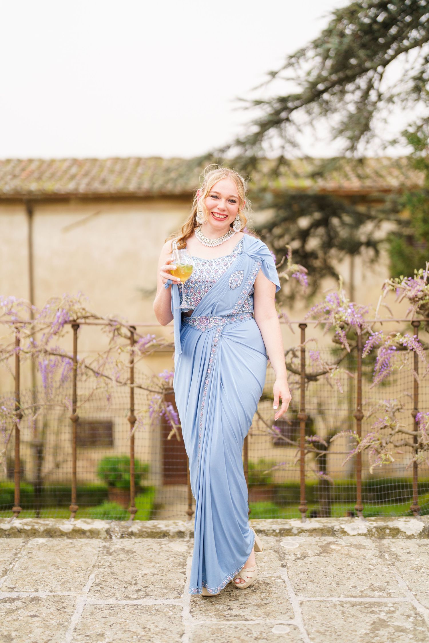 Person in light blue dress posing gracefully against rustic Italian villa backdrop.