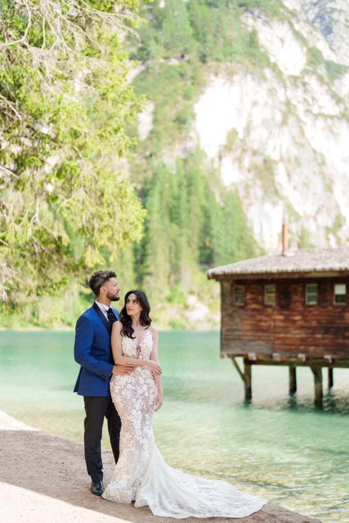 A romantic wedding photoshoot by a wooden boathouse on a turquoise alpine lake with dramatic mountain cliffs.
