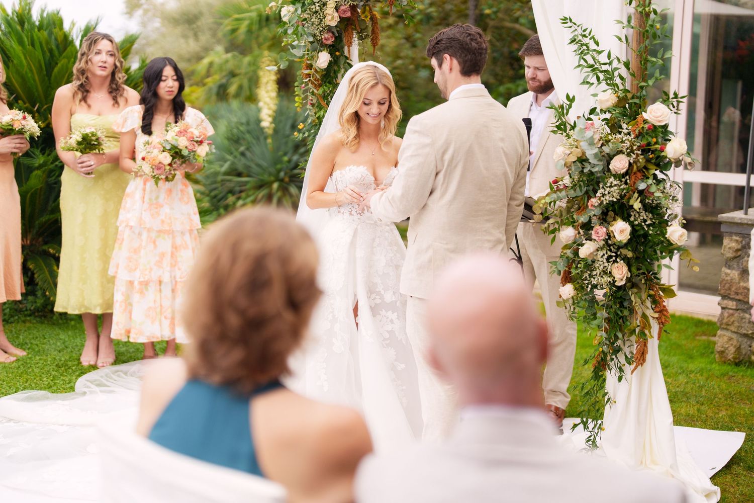 Elegant wedding ceremony setup with floral arch and white chairs on a manicured lawn.
