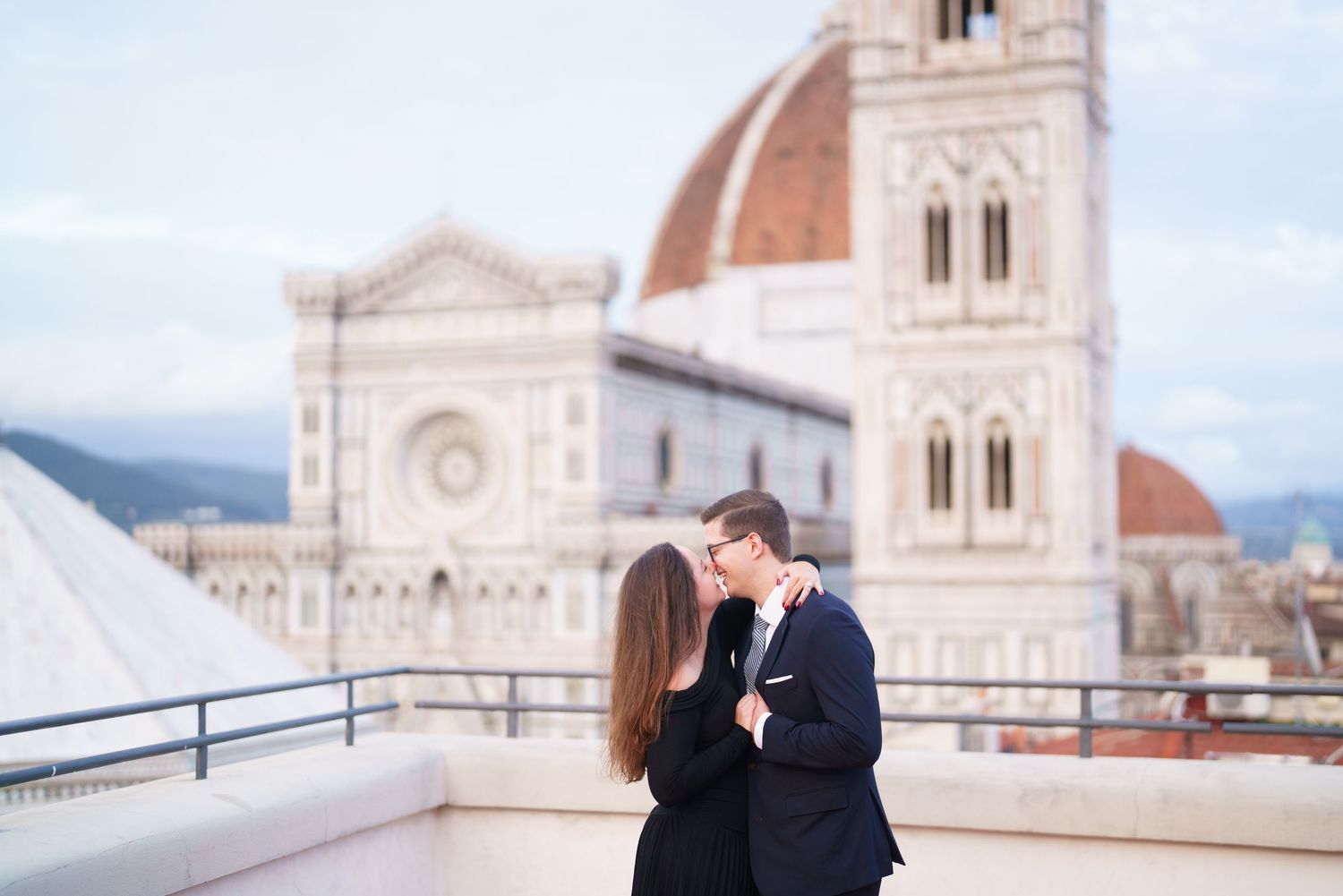 A couple embraces in front of the Florence Cathedral in Italy, with the historic Duomo visible in the background.