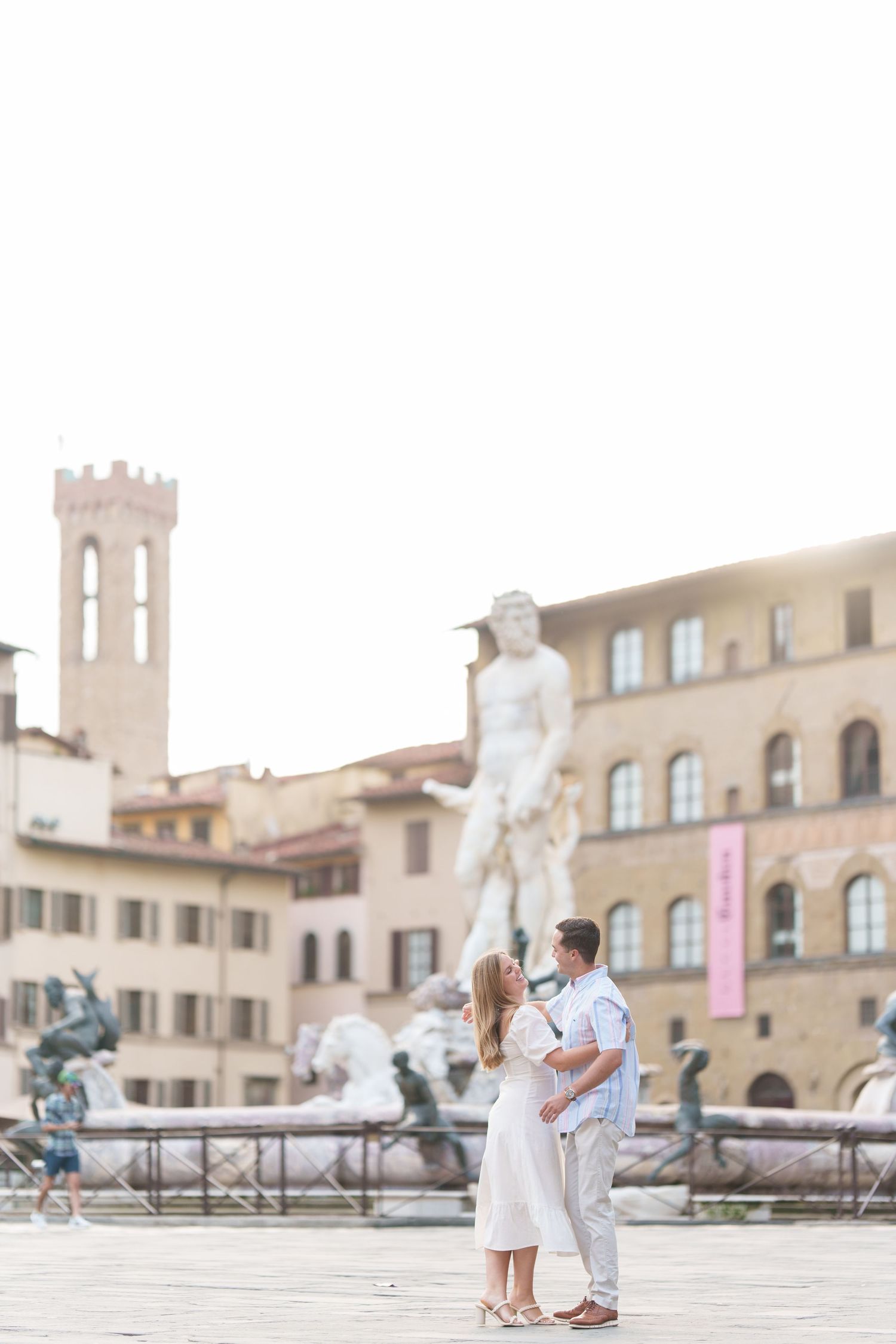 Romantic couple embraces in Florence's Piazza della Signoria with Neptune Fountain and historic architecture in background.