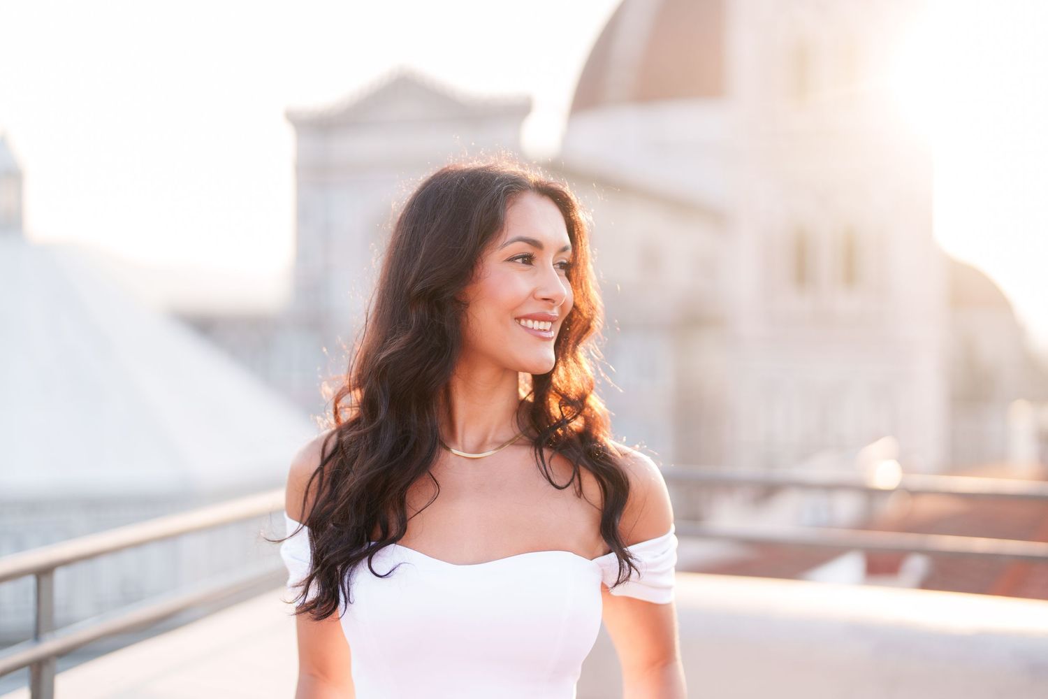 A woman in a white dress walks along a sunlit path with a warm glow in the background.