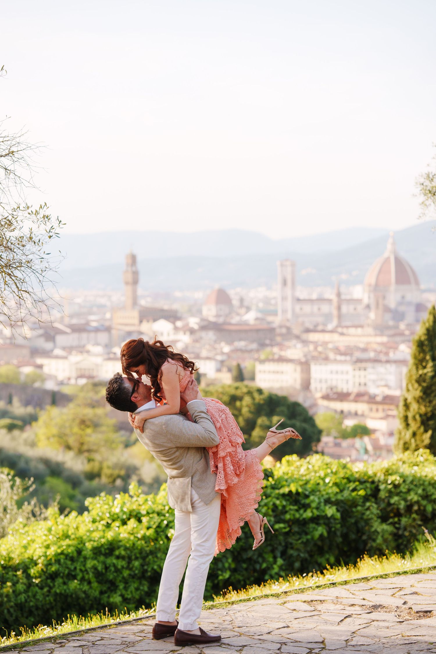 A romantic couple shares a passionate embrace overlooking the stunning cityscape of Florence, Italy from Piazzale Michelangelo.