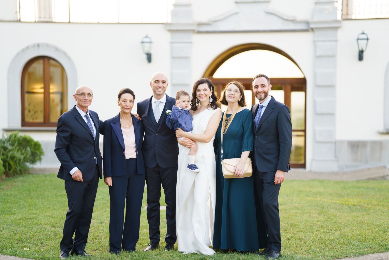 Wedding party poses together in formal attire outside white building.