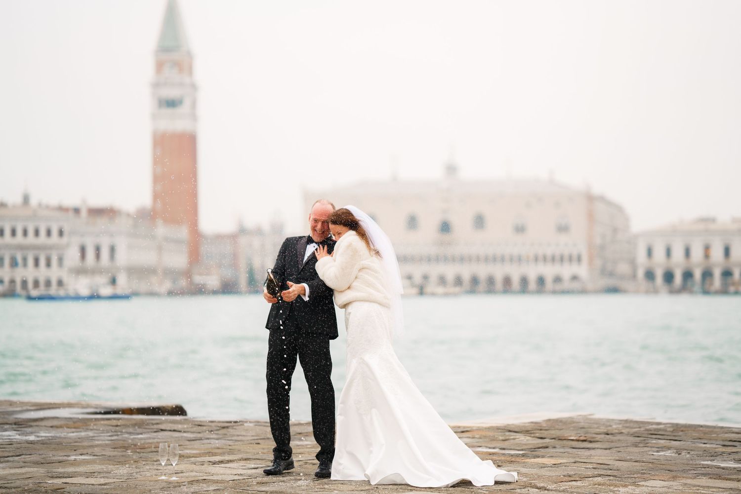 A couple in wedding attire shares an intimate moment along the Venice waterfront with historic buildings in the background.