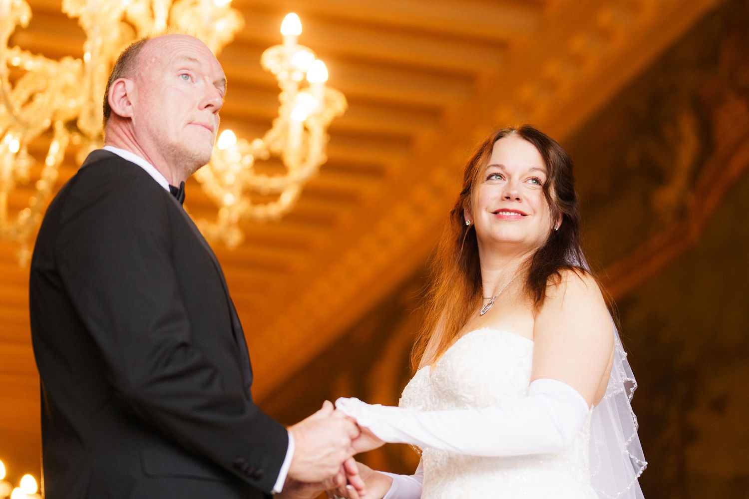 A bride and groom dance together during their first dance at an elegant reception with warm glowing chandeliers overhead.