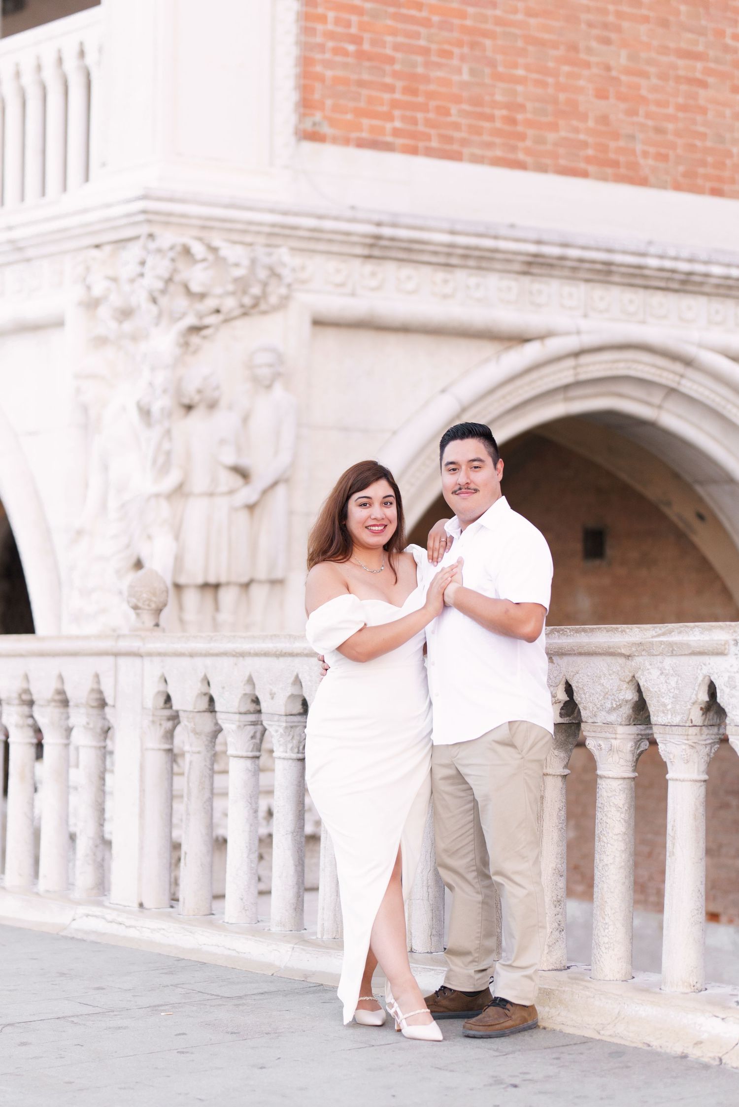 A romantic couple poses together against an ornate stone archway and columns in an elegant architectural setting.