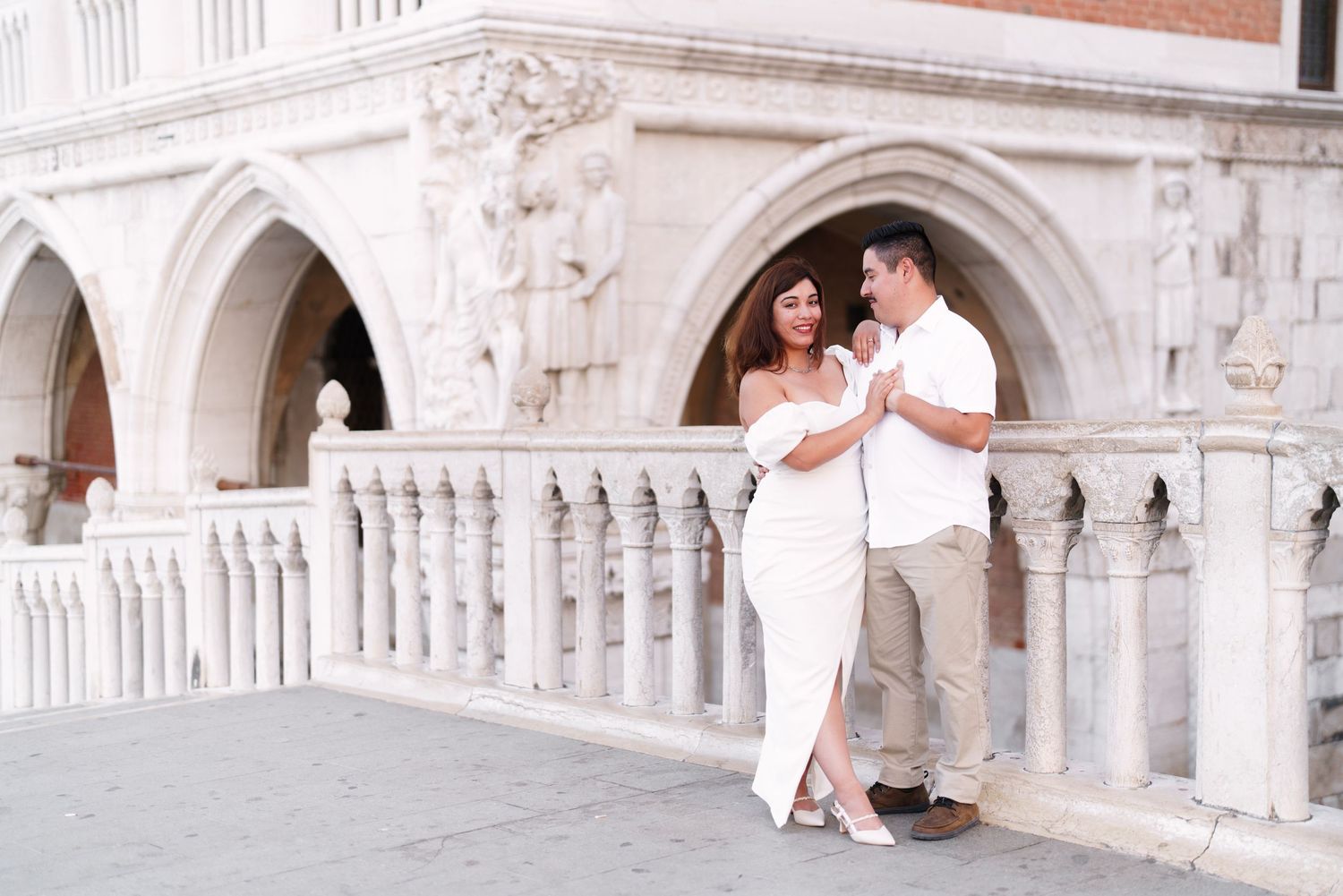 Romantic couple in elegant wedding attire share intimate moments along Venice's iconic Doge's Palace colonnade.